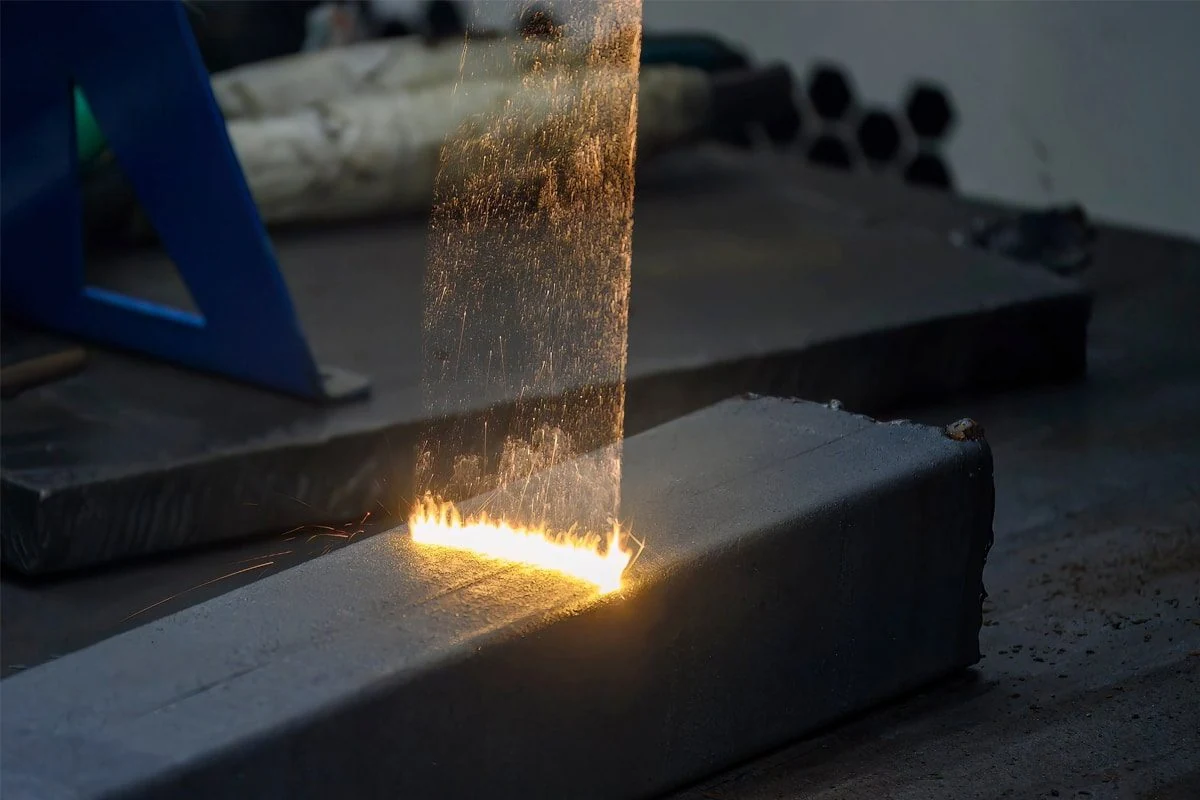 Laserstraal reinigt een donkere metalen balk in een werkplaats, met vonken boven het oppervlak